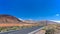 Speed limit signs on asphalt road disappearing over the horizon through volcano mountain hillsides. White clouds on a blue sky. La