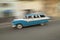 A speeding blue and white 1955 Ford station wagon driving through the streets of Havana, Cuba