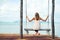 Spending the day in paradise. Shot of a young woman sitting on a swing overlooking the ocean.