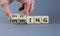 Spending or investing symbol. Businessman turns cubes and changes the word `investing` to `spending`. Beautiful grey table, gr