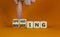Spending or investing symbol. Businessman turns cubes and changes the word `investing` to `spending`. Beautiful orange table,