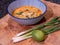 Spicy asian coconut soup with red curry paste, served in a blue bowl on a wooden block with spring onions, lime and chili flakes