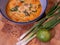 Spicy asian coconut soup with red curry paste, served in a blue bowl on a wooden block with spring onions, lime and chili flakes