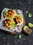 Spicy bean tostadas with corn salsa and avocado on a rustic cutting board on a dark background.