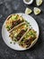 Spicy beef and cabbage, carrots pickled salad tacos on dark background, top view