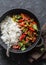 Spicy beef with vegetables and rice in a cast iron skillet on a dark background, top view.