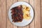 Spicy hot grilled spare ribs from BBQ top view served on a plate with paprika scalloped potatoes on rustic wood table.