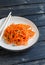 Spicy pickled carrot salad in an asian style on a white plate on a dark wooden background.