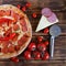 Spicy pizza with red chili pepper and salami lies on a wooden table next to a special circular knife, a branch of tomatoes, sliced