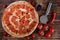 Spicy pizza with salami and pepperoni lies on a wooden surface next to a special circular knife, tomatoes, red pepper and barbecue