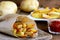 Spicy potato fries. Baked sweet potato fries in paper and white plate, spicy tomato sauce, raw potato on a wooden table. Closeup