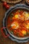 Spicy shakshuka in a pan with parskey , bread and hummus, close view