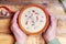 Spicy soup with sour cream, bread and spices on burned wooden table. Traditional rural dinner. Old woman hands holds clay bowl