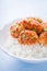 Spicy sweet and sour chicken with sesame and rice on blue wooden background close up