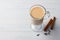 Spicy warming tea with milk in glass cup with cinnamon sticks and cloves on light gray blue background