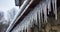 Spiked Icicles Dangling from a Pitched Gray Roof, Adorned with Snow Clumps, Against a Stone-Walled House