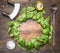 Spinach leaves have been laid out around a circular chopping board, with herbs and salad spoon, knife and salad, frame, space for