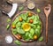 Spinach leaves have been laid out around a circular chopping board, with herbs and salad spoon,knife and salad, salt, pepper, che