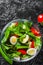 Spinach salad with eggs, pepper and tomatoes in glass bowl on dark