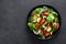 Spinach salad with fresh cucumbers, tomato, onion, pomegranate, sesame seeds and cashew nuts on black background. Healthy vegan fo