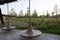 Spinning wooden bench and metal pergola. Walkway with grass lawn, bushes, plants, trees in background. Tyufeleva Roshcha city park