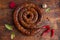 Spiral sausage ring baked in an old oven is on a wooden board with pepper and garlic