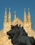 Spires of the Duomo Cathedral in Milan with a lion in the foreground, which is part of the statue of Victor Emmanuel II