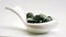 Spirulina chlorella pills falling into white spoon.