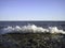 A splash of sea water on a stone pier with lots of foam and spray on a Sunny day against a flat horizon