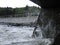 A splash of seawater under a stone Pier with lots of foam and spray against the background of a shingle beach and city promenade