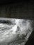 A splash of seawater under a stone Pier with lots of foam and spray against the background of a shingle beach and city promenade