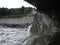 A splash of seawater under a stone Pier with lots of foam and spray against the background of a shingle beach and city promenade