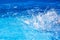 Splashes of clear blue fresh water in pool, air bubbles, water drops, sea wave on blue background with sunny reflections