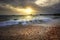 splashing sea wave on gravel beach against sun set sky and commercial ship port