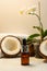 Split coconuts with coconut essential oil. Coconut serum for the face. A bottle of whey oil with a pipette on a white-beige