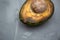 Spoiled avocado with green mold and black spots of rot and fungus on a gray background. Cut natural fruit, half with a round bone.