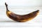 A spoiled darkened banana stands on a white background