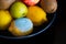 Spoiled lemon with light blue textured mold among ripe colorful whole fruits: apples, kiwi, edible yellow lemons in a plate.