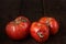 Spoiled three tomatoes on a dark wooden background.