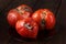 Spoiled three tomatoes on a dark wooden background.