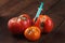 Spoiled three tomatoes with stuck syringe on a dark wooden background.