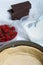 Sponge cake in a baking dish. Coconut flakes and cream in a container. Nearby are raspberries and pieces of chocolate. Levington