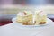 Sponge cakes soaked in brandy lie in a white plate next to scattered macadamia nuts and walnuts on a light background. Wooden