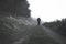 A spooky blurred ghostly hooded figure on a path in the countryside on a foggy day. With a muted, grainy edit