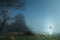 A spooky, blurred, glowing, ghostly woman with a white dress, standing in a field. On a spooky winters night