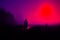 A spooky concept. Of a hooded figure silhouetted against the moon in the countryside at night. With a neon vapor wave edit