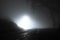 A spooky, eerie country road passing through a hill. With a light in the distance. On a mysterious foggy, winters night