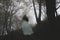 A spooky ghostly woman in a long white dress walking up a path through a moody misty autumn woodland