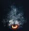 Spooky Halloween jack o lantern pumpkin with carved scary grinning face glowing in smoke on Halloween night