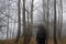 A spooky hooded figure with a blurred head, standing in a moody foggy wood in winter